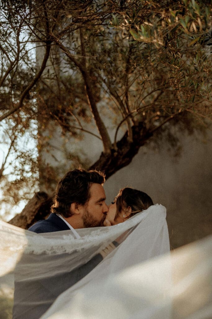 Romantic veil portrait of a newlywed couple sharing a kiss during golden hour at a Destin, Florida wedding, photographed in a cinematic, film-inspired documentary style.