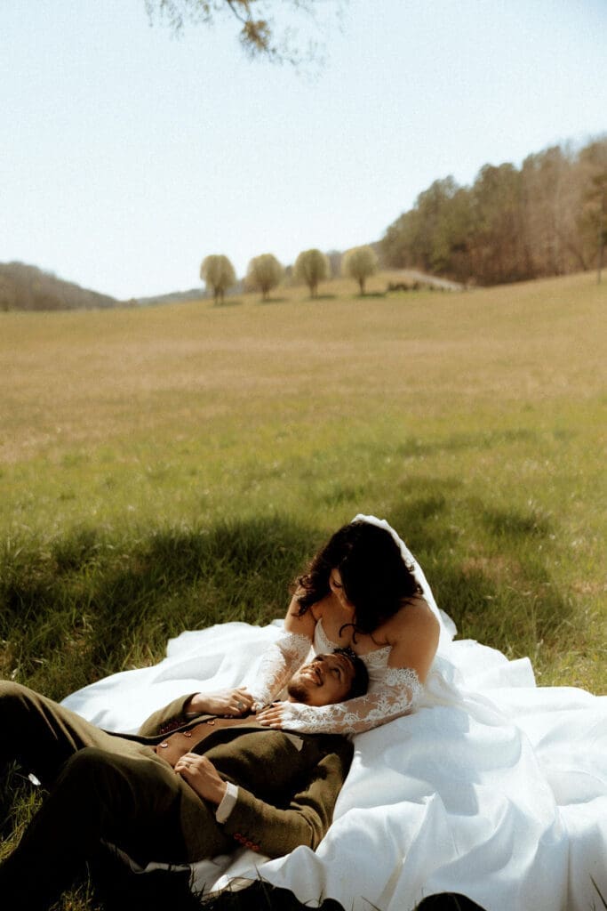 Bride cradles her groom as they relax in the grass after their wedding ceremony in Wildwood, Georgia, captured in a romantic, film-inspired documentary style.