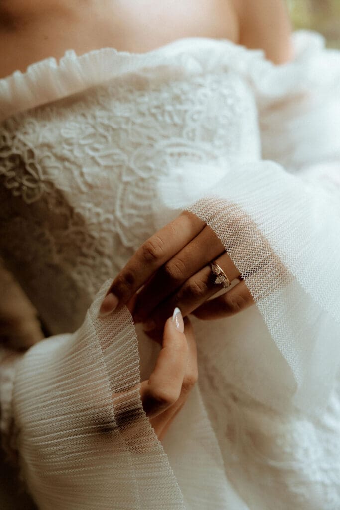 Close-up of a bride’s engagement ring and lace wedding dress as she gently holds her veil during a wedding day in Atlanta, Georgia, captured in a romantic, film-inspired style.