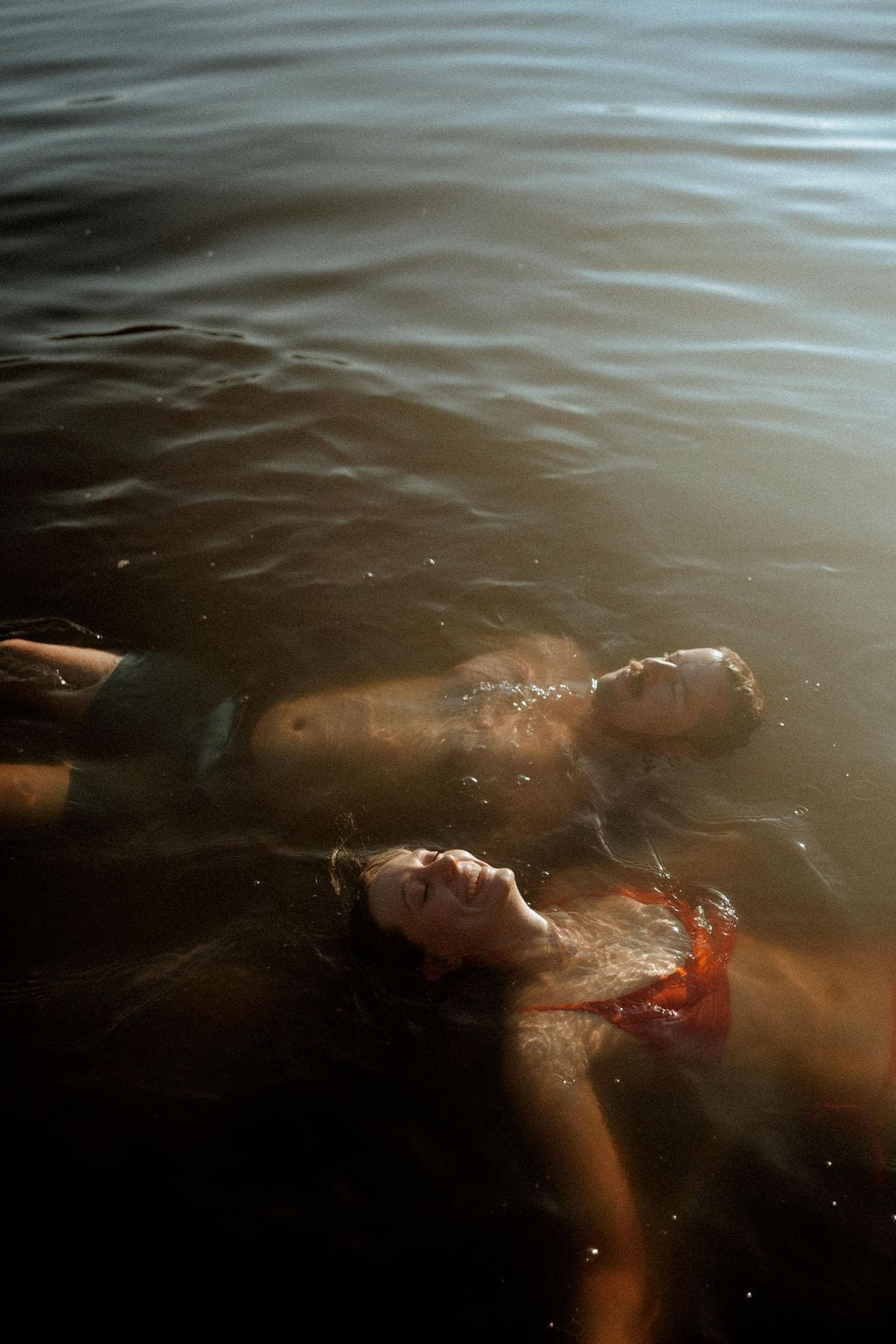Couple floating together in a lake during a golden hour couples session near Mobile, Alabama.